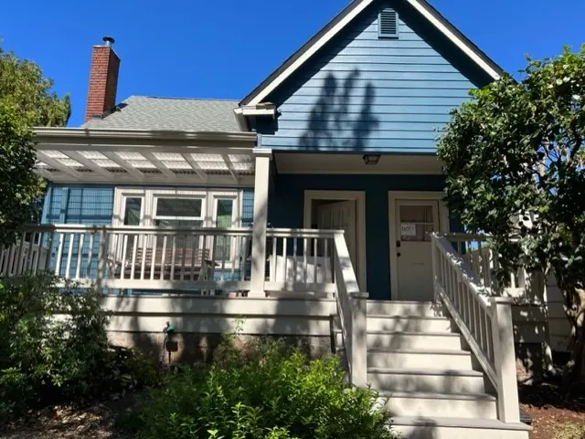 Blue bungalow with a white porch railing and brick chimney