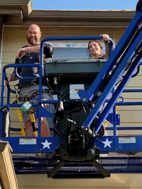 Two people on a boom lift at a siding job